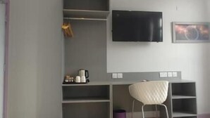 A room with a desk, chair, TV, and shelving units. - London Croydon Hotel (Thornton Heath)