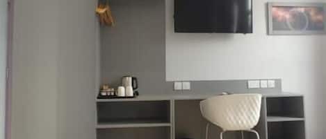 A room with a desk, chair, TV, and shelving units.