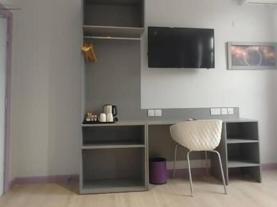 A room with a desk, chair, TV, and shelving units.