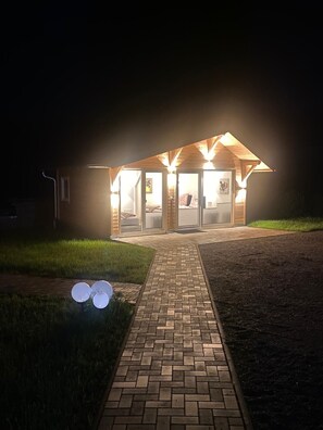 Un bâtiment avec un chemin en briques menant à une structure en bois dotée de portes et de fenêtres en verre.