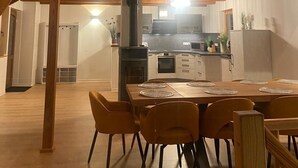 Een ruime loft met een hoge plafond, houten balken, een eethoek met tafel en stoelen, en een keuken met moderne apparatuur.