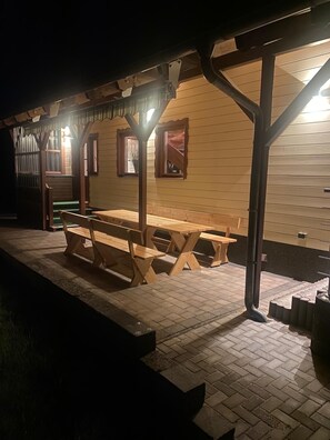 Un pavillon en bois installé à l’extérieur, avec des tables de pique-nique et des bancs, une allée couverte et, au fond, un bâtiment doté de fenêtres et d’une porte.