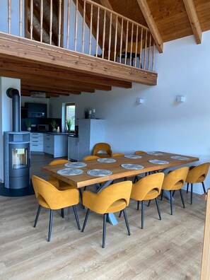 Une cuisine moderne dotée d’une cuisinière intégrée, un coin repas avec une table en bois et des chaises jaunes, et un escalier menant à un niveau supérieur.