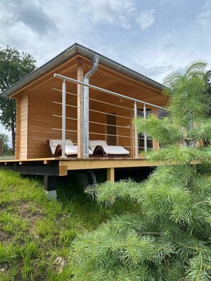 Une cabane en bois moderne dotée d’un balcon, d’une rambarde en métal et d’une cheminée.