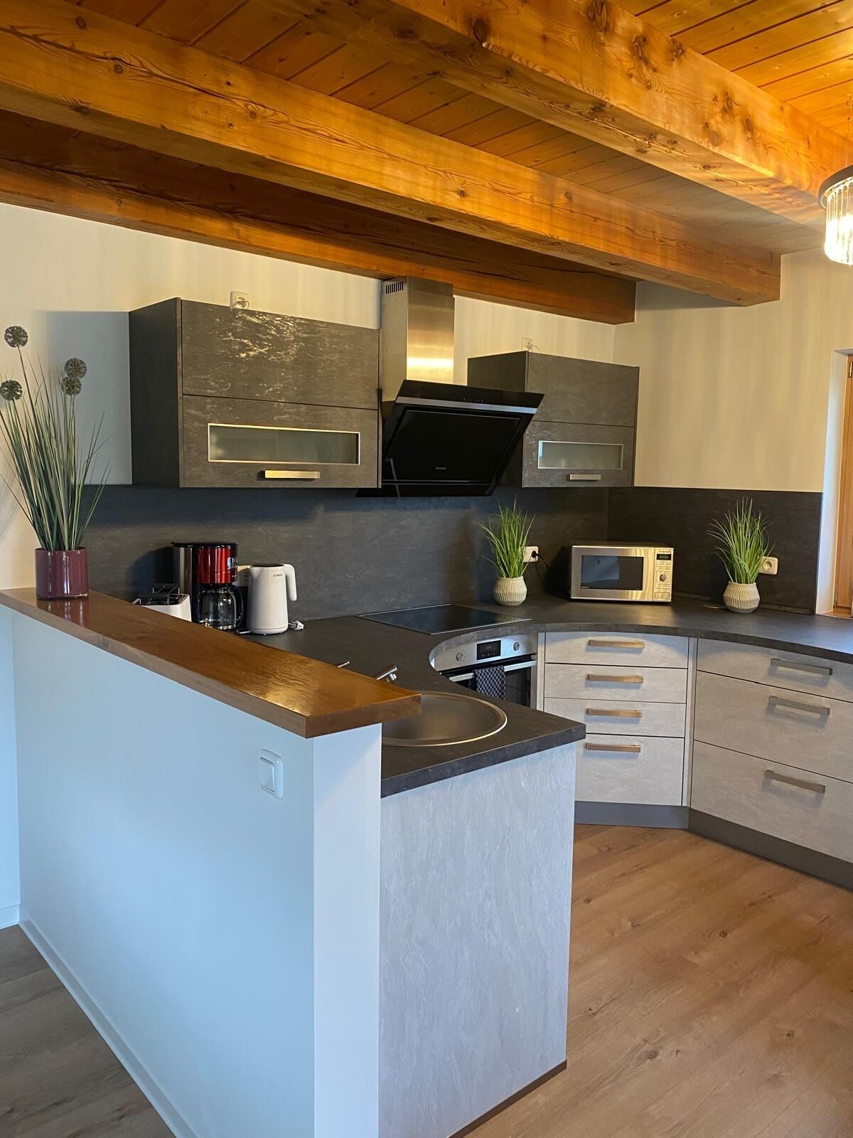 A modern kitchen with a central island, built-in appliances, and wooden ceiling beams.