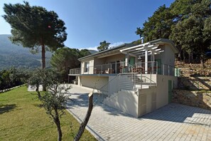 Ein zweigeschossiges Haus mit Balkon, Steinmauer und Blick auf die umliegende Landschaft.