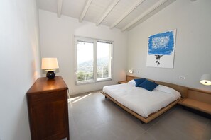 Ein Schlafzimmer mit einem Bett, einem Nachttisch, einer Kommode, einem Fenster mit Blick und einem Wandbild.