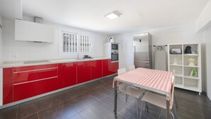 Una cucina moderna con mobili rossi, un piano di lavoro bianco e una zona pranzo con tovaglia a quadri.