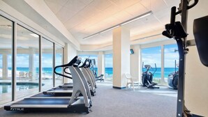 A modern gym with treadmills, stationary bikes, and a rowing machine, overlooking a beach. - Beachfront- Amazing Views-Lighthouse 310 (Gulf Shores)