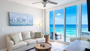 A spacious living room with a large window offering a view of the ocean, a ceiling fan, a sofa, a coffee table, and a television. - Beachfront- Amazing Views-Lighthouse 310 (Gulf Shores)