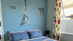 A bedroom with a bed, a wall with a Paris-themed mural, a window with curtains, and a nightstand. - North east valley apartment (Dunedin)