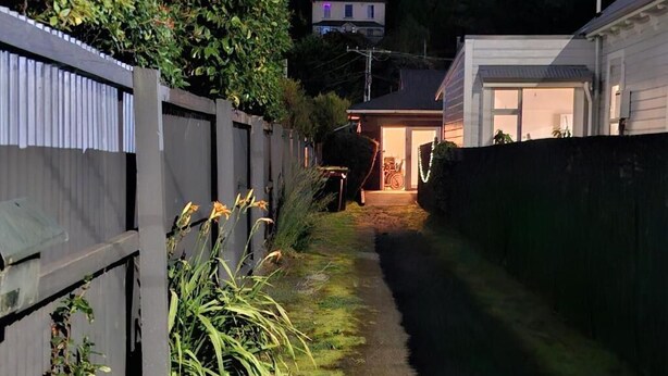 A narrow pathway leading to a house with a visible garage door and a small porch area. - North east valley apartment (Dunedin)