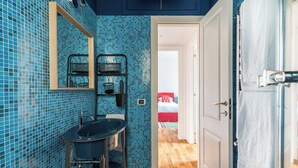 A bathroom with blue mosaic tiles, a sink, a mirror, and a shower area.