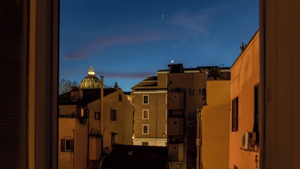 A narrow street with buildings, a dome structure, and a crescent moon in the sky.