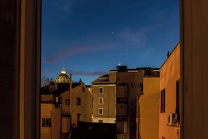 Rua estreita com edifícios, uma estrutura em cúpula e uma lua crescente no céu.