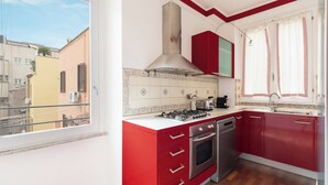 A compact kitchen with red cabinets, a gas stove, an oven, and a stainless steel range hood.