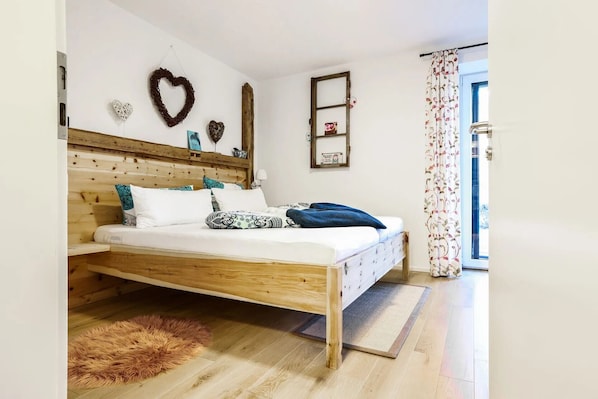 A bedroom with a wooden bed, a fluffy rug, heart-shaped decorations, and a window with floral curtains.