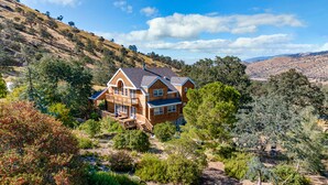 A large, two-story house with a balcony, surrounded by trees and hills. - Spacious Family Cabin w/Hot Tub & Mountain Views (Tehachapi)