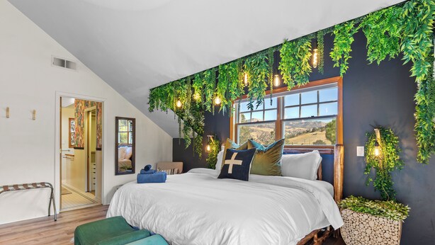 A bedroom with a large bed, a wooden floor, a window with a view, and a plant wall. - Spacious Family Cabin w/Hot Tub & Mountain Views (Tehachapi)