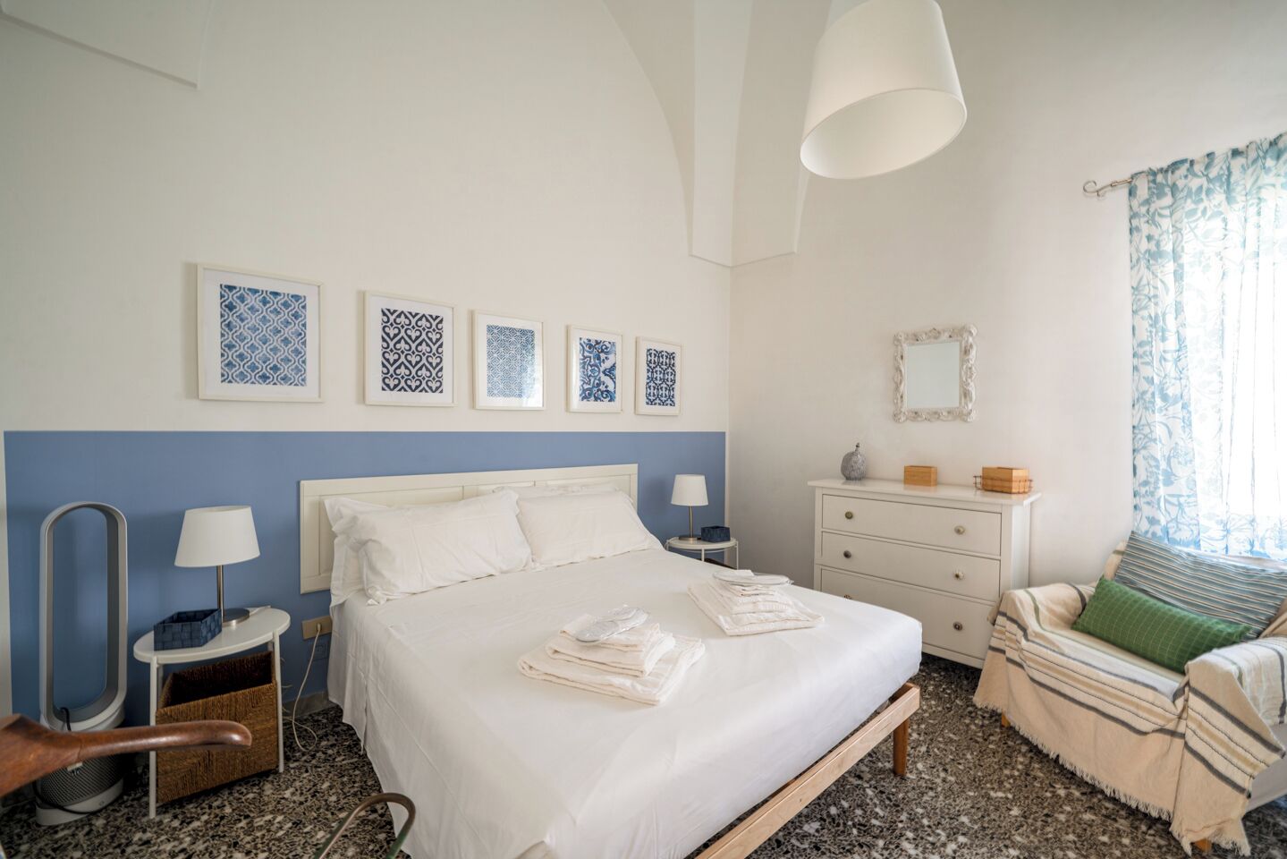 A bedroom with a bed, bedside tables, a dresser, a mirror, and wall art.