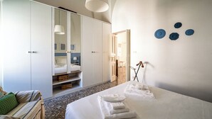 Een slaapkamer met een bed, een kledingkast, een spiegel en een deur naar een andere kamer.