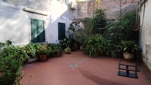 A courtyard with potted plants, a swing, and a white building with green shutters. - Gatto errante (Pesaro)