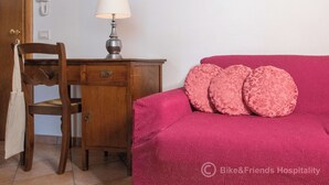 A room with a wooden desk, a lamp, a chair, and a bed with pink pillows. - Gatto errante (Pesaro)