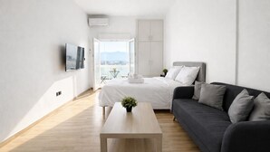 A modern, minimalist bedroom with a bed, a dark sofa, a wooden coffee table, and a TV mounted on the wall. - Athens View Studio Near Lycabettus Hill by MPS (Athina)