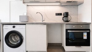 A compact kitchen with a washing machine, a coffee maker, and an oven. - Athens View Studio Near Lycabettus Hill by MPS (Athina)