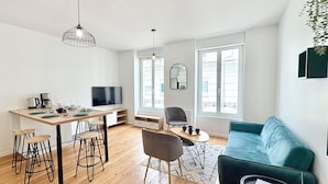 Un espace de vie moderne comprenant un coin repas, un canapé, un téléviseur et un ordinateur portable posé sur une table.