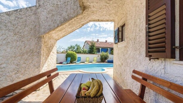 Ein Steinhaus mit Pool, Holzliegen und einem Obstkorb.