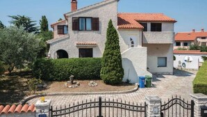 Ein zweigeschossiges Haus mit einer Stein-Fassade, einem Ziegeldach und einer umzäunten Auffahrt.