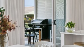 Eine offene Terrasse mit Grill, Esstisch, Stühlen und einem Blumentopf.