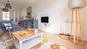 A living room with a blue chair, a wooden coffee table, a television, a radiator, and a tall floor lamp. - Holiday Home “Captiva” with Wi-Fi (Saint-Georges-d'Oléron)