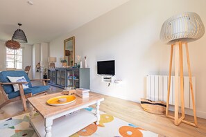 A living room with a blue chair, a wooden coffee table, a television, a radiator, and a tall floor lamp. - Holiday Home “Captiva” with Wi-Fi (Saint-Georges-d'Oléron)