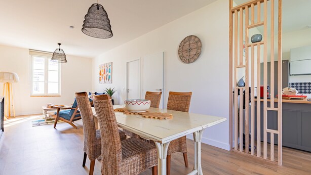 A dining area with a white table, wicker chairs, and a large wall clock. - Holiday Home “Captiva” with Wi-Fi (Saint-Georges-d'Oléron)