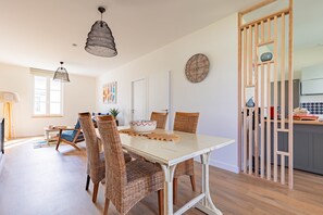 A dining area with a white table, wicker chairs, and a large wall clock. - Holiday Home “Captiva” with Wi-Fi (Saint-Georges-d'Oléron)