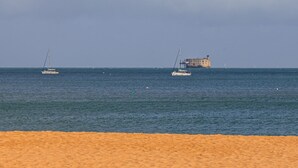 A beach with a sandy foreground and calm sea. In the distance, there is a large building with a tower. - Holiday Home “Captiva” with Wi-Fi (Saint-Georges-d'Oléron)