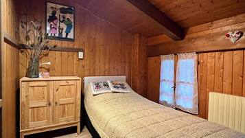 A wooden-paneled room with a bed, a wooden cabinet, a vase with dried flowers, and a painting on the wall.