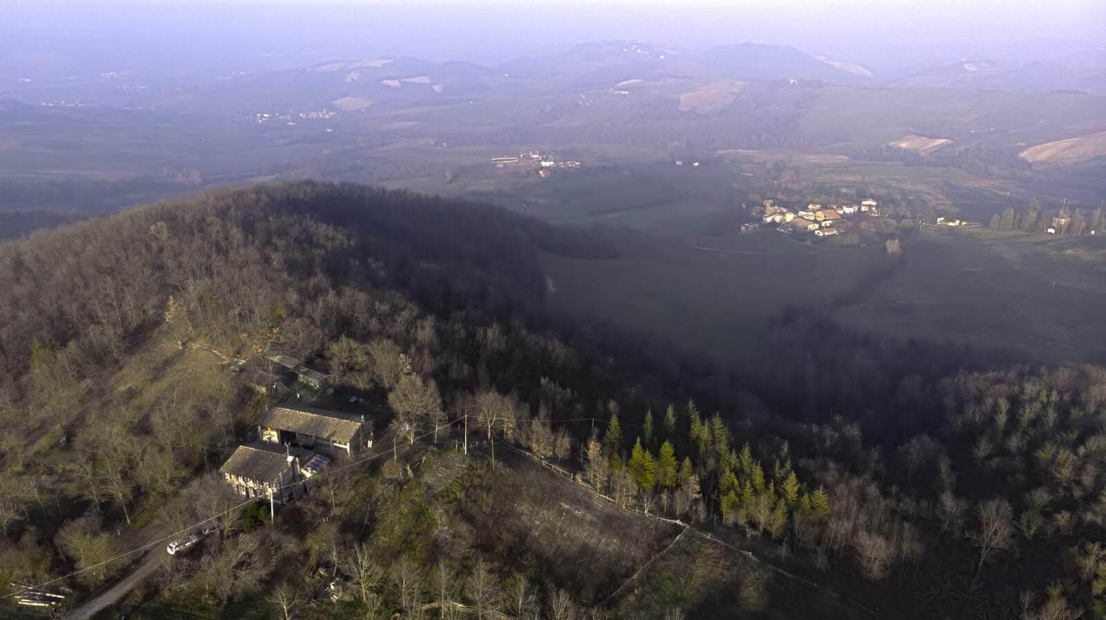 Vista aerea di una zona rurale con un piccolo edificio circondato da alberi e campi aperti.