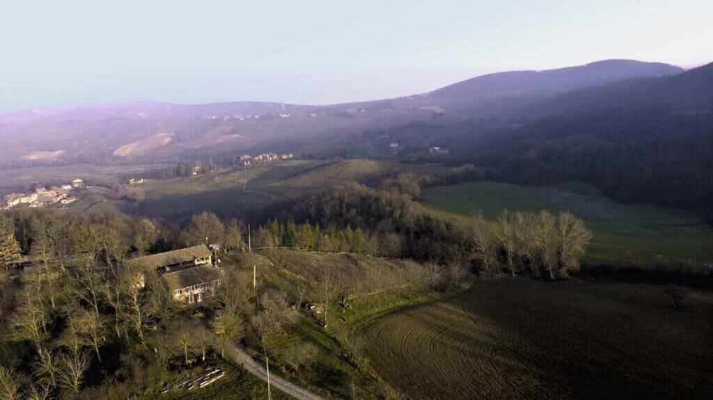 Vista aérea de un paisaje rural con colinas onduladas, algunas casas dispersas y un cielo despejado.