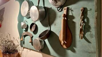 Una cucina con diverse pentole e padelle appese al muro, un mattarello di legno e un cesto di vimini con fiori secchi.