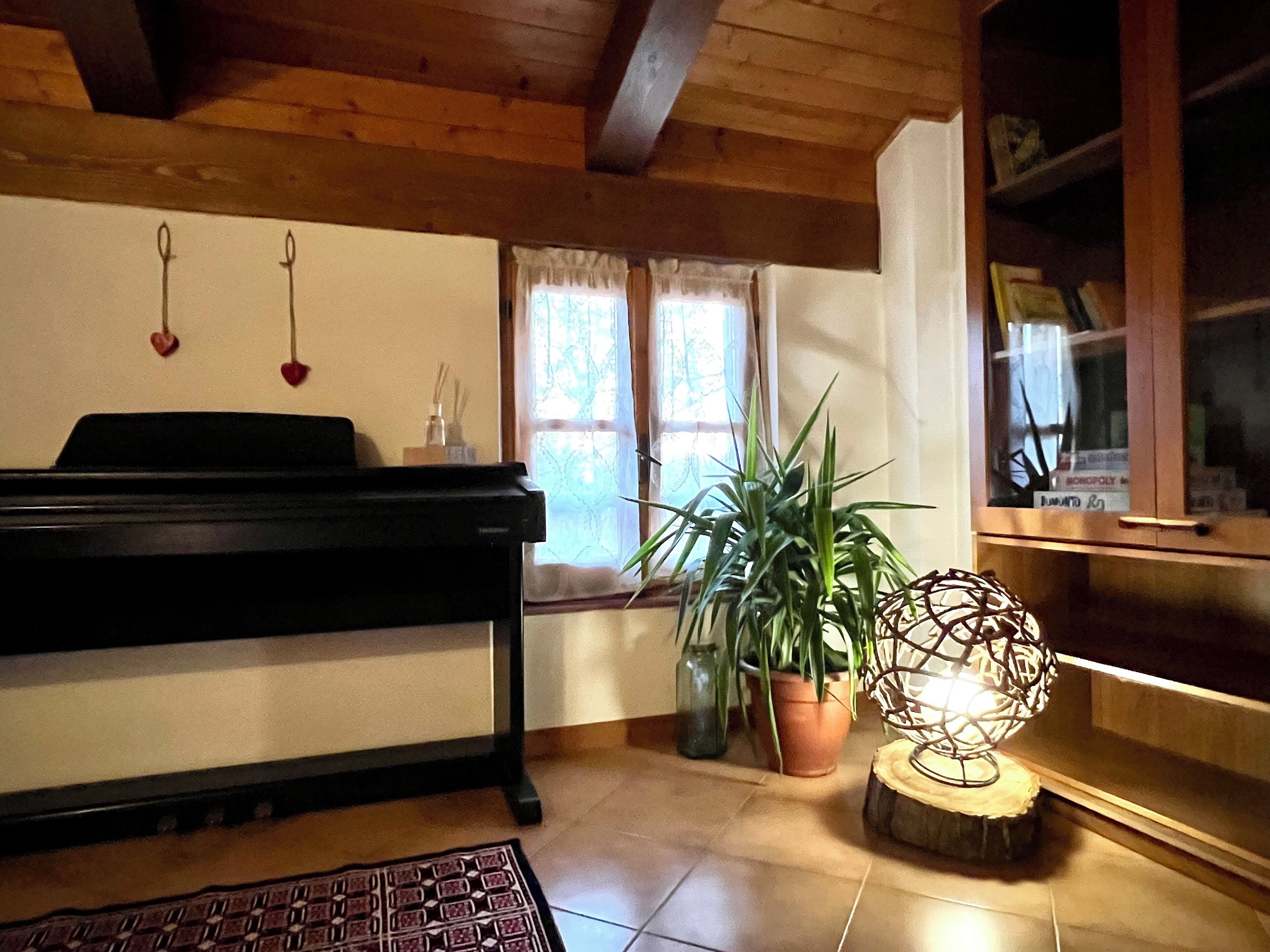 Una stanza con un pianoforte, una pianta in vaso, una lampada decorativa e una finestra con tende.
