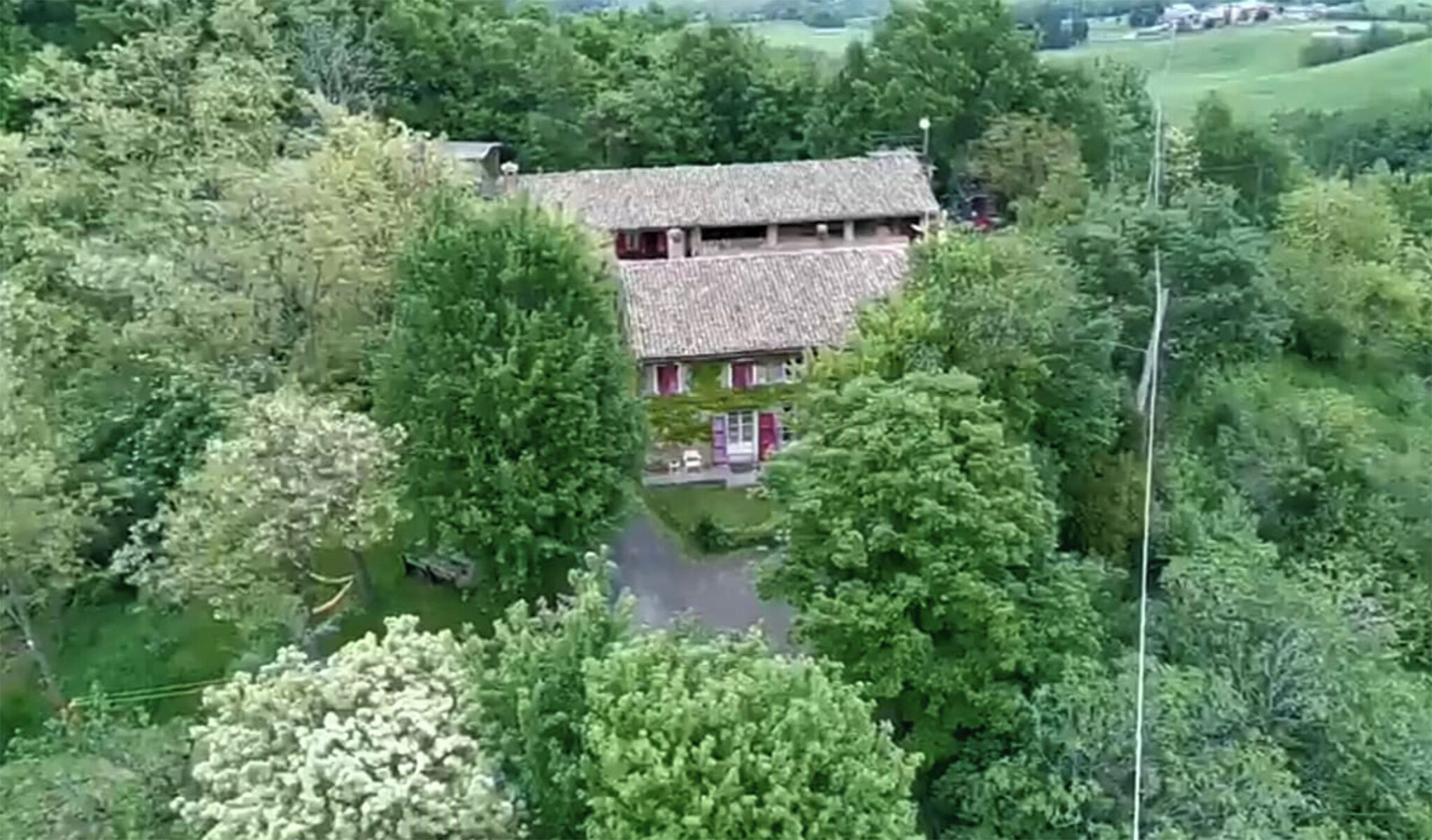 Une maison à deux étages, entourée d’une végétation luxuriante, avec une allée bien visible menant à l’entrée.