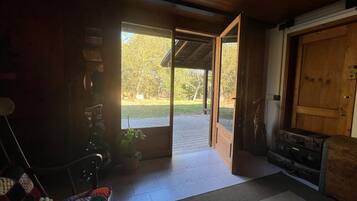 A cozy room with a wooden ceiling, a large open door leading outside, a wooden bench, and a small table with a plant.