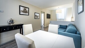 Ett modernt hotellrum med ett matbord, två stolar, en soffa, ett skrivbord med en lampa och inramade tavlor på väggarna.