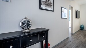 En hall med ett svart konsolbord, en inramad tavla, en väggklocka och en brandsläckare.
