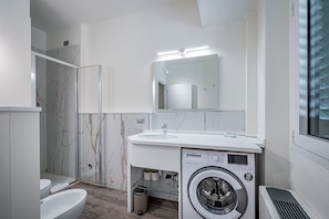 Une salle de bain moderne avec une douche en marbre, un lavabo, un miroir et un lave-linge.