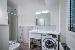A modern bathroom with a marble shower, a sink, a mirror, a washing machine, and a toilet. - Garibaldi Palace trilo Art Coll 2 (Prato)