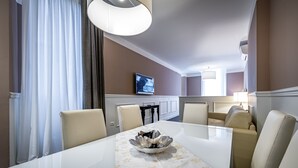 Un comedor con una mesa blanca, sillas color beige, un cuenco decorativo y un televisor en la pared.